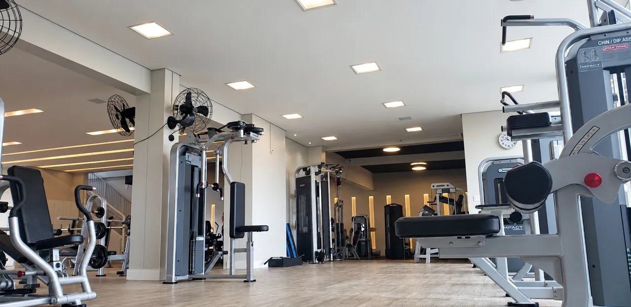 Salão de musculação com máquinas de carga guiada e luz de teto embutida