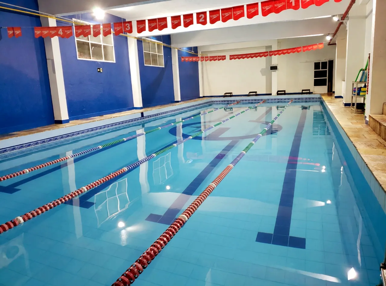Piscina coberta de raias, com paredes azuis, bandeirinhas numeradas e a marca da Estilo no fundo